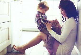 Mother with her baby playing with pet on the floor at the kitchen at home